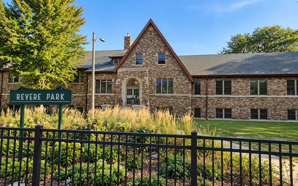 The stone Revere Park fieldhouse behind its entrance sign and garden beds